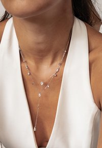 Srebrna naszyjnik z warstwą, zdobiony kryształowymi akcentami w kształcie kropli i okrągłymi, z subtelnym wzorem łańcuszka i układem w kształcie litery V wisiorka.
