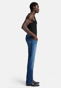 Blå denimjeans med rak ben(ben)stammar, bärs med en svart linne. Funktioner inkluderar fram- och bakfickor, samt sydda detaljer. Svarta stövlar.