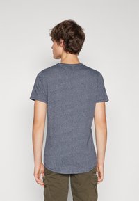 Mörkblå t-shirt med kort ärm och rund halsringning, slät textur och rundad fåll. Bärs med ljus olivgrön cargobyxor.