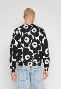 Svart og hvit blomstermønstrete genser med rund hals, ribbestrikkede cuffs og nederkant, brukt med lyseblå jeans.