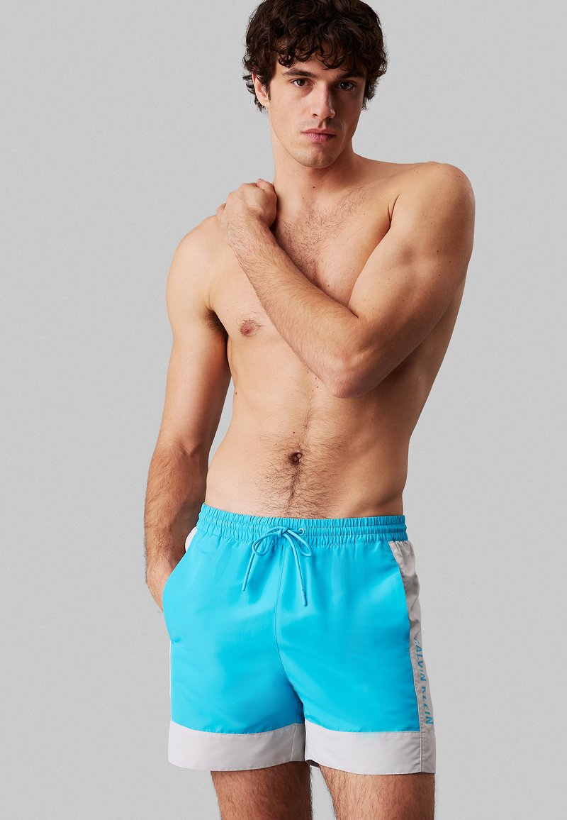 Pantaloncini da bagno turchese con dettaglio bianco all'orlo, vita elasticizzata con coulisse, con logo laterale.