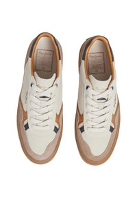 Zapatillas de ante blancas con acentos en marrón y azul marino. Presentan una puntera redonda, cordones planos y una suela de goma texturizada. Logo en el lado y en la lengua.