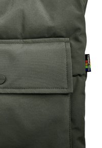 Donkergroene, gewatteerde stof met een rechthoekige zak die is beveiligd met een drukknoop en een klein, multikleurig Thermo Tech-label aan de zijkant.