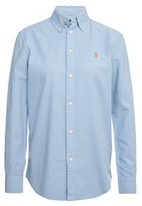 Camicia azzurra chiara con bottoni in cotone, dotata di colletto a punta, bottoni bianchi e un piccolo logo rosso sul petto sinistro.