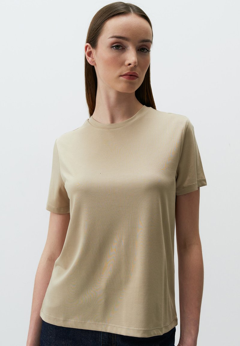 T-shirt beige a maniche corte realizzato in tessuto morbido, con scollatura rotonda e vestibilità comoda. Design semplice senza motivi o decorazioni.