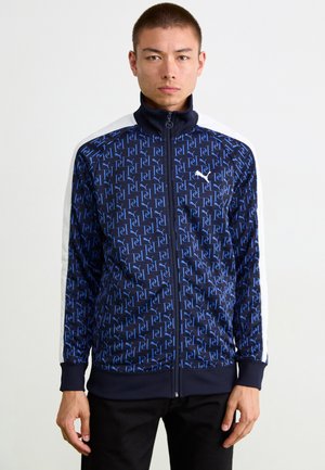 Marinekleurige ritsjack met herhalend blauw logo-patroon, witte zijkanten, hoge kraag en ribgebreide manchetten en onderkant. Zacht, glad materiaal.