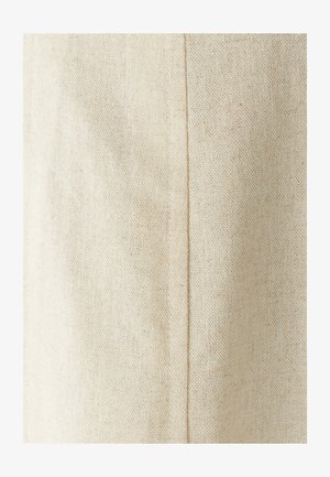 Tela de algodón beige con un tejido texturizado; presenta una costura visible que corre verticalmente. Textura ligeramente áspera con un acabado natural.