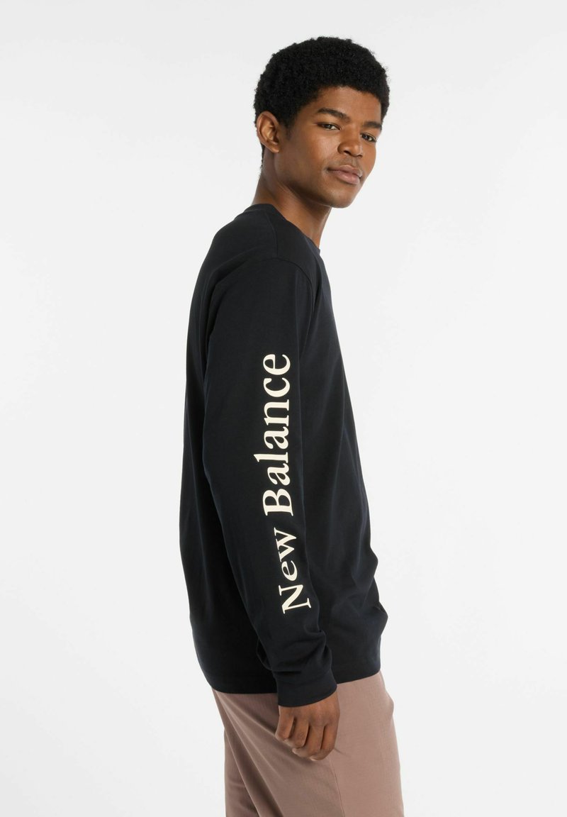 Zwarte longsleeve shirt met het "New Balance" logo in lichte kleur gedrukt langs de rechter mouw. Katoenen materiaal, fitted ontwerp.