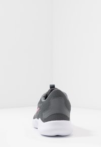 Grijze sportschoen met een gestructureerde mesh bovenkant, contrasterend roze logo, treklus bij de hiel en een witte rubberen buitenzool. Achteraanzicht getoond.