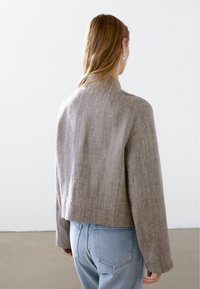 Gray textured cropped jacket with long sleeves, made of a woven fabric, paired with light blue denim jeans. Simple, clean design.