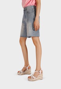 Gonna di jeans con orlo sfrangiato e decorazioni a forma di cuore, abbinata a sandali con zeppa bianchi e fibbie, caratterizzati da una piattaforma testurizzata.