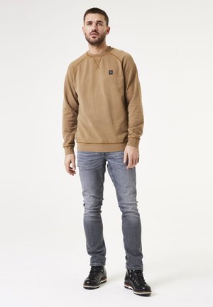 Brown fleece sweatshirt with a round neck, ribbed cuffs, and hem. Paired with light blue jeans and black, lace-up boots.
