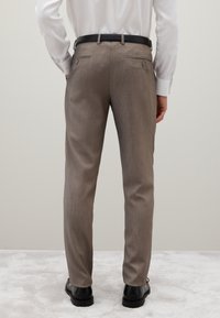 Braune maßgeschneiderte Hosen aus strukturiertem Stoff, ausgestattet mit zwei Gesäßtaschen und einem schwarzen Gürtel. Der Schnitt ist schmal mit gerader Beinform.