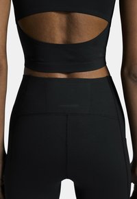 Haut de sport noir court avec un dos ouvert, associé à un legging noir taille haute, présentant des coutures élégantes et une finition lisse et texturée.