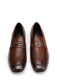 Chaussures marron en cuir à enfiler avec un design perforé, présentant un accent de boucle décorative. Texture lisse avec une forme de bout carrée.