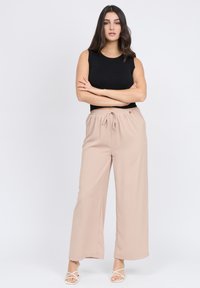 Top nero senza maniche, pantaloni larghi beige con vita elasticizzata e cordoncino, texture liscia, posizionati su uno sfondo bianco.