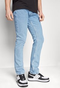 Jeans de mezclilla azul claro con corte recto, que cuentan con bolsillos frontales y detalles cosidos, combinados con zapatillas deportivas en blanco y negro.