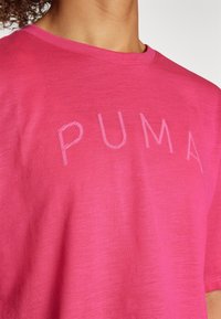 Camiseta de algodón rosa con cuello redondo y una superficie ligeramente texturizada, con el logotipo de "PUMA" bordado en un tono más claro.