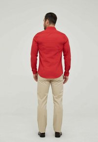 Chemise rouge à manches longues, design ajusté, texture lisse, associée à un pantalon beige clair, fabriqué dans un matériau léger. Style simple et classique.