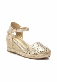 Alpargata cuña en dorado metálico con diseño perforado. Cuenta con una suela de yute trenzada y una correa en el tobillo con cierre de hebilla.