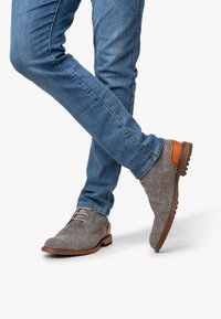 Scarpe grigie a spina di pesce con dettagli in pelle marrone, design con lacci e suole in gomma robuste, abbinate a jeans blu.