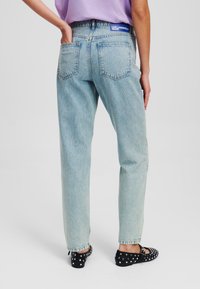 Lichtblauwe high-waisted jeans met een rechte snit, voorzien van achterzakken en een merkband. G draagt met zwarte met studs versierde flats.