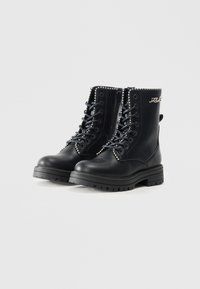 Botas de tornozelo pretas com atacadores e sola grossa, apresentando tachas metálicas ao longo da borda superior e um fecho de correr lateral para facilitar o calçar.