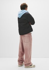 Sort pufferjakke med lyseblå hætte, parret med falmede lyserøde vide bukser og beige sneakers med grønne detaljer.