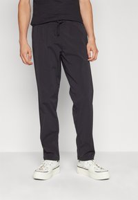 Mørkegrå, letvægtsbukser med elastisk talje og snor. At parre dem med hvide sneakers tilføjer kontrast til outfittet.