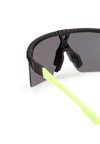 Ochelari de soare sport negri cu un design înfășurător, lentile gri și brațe de tempă verzi vibrante, cu texturi antiderapante pentru stabilitate.