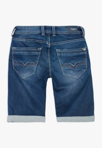 Siniset farkushortsit käännetyillä lahkeilla, takataskut koristeompeleilla ja nahkabrändipatchilla vyötäröllä.