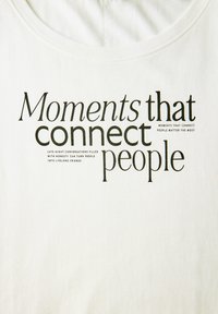 Bílý bavlněný tričko se černým textem: "Momenty, které spojují lidi" s dalším menším textem níže. Jednoduchý, neformální design.