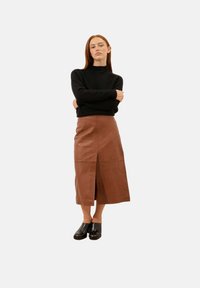 Brązowa skórzana spódnica midi z rozcięciem z przodu, zestawiona z czarnym swetrem. Gładka tekstura, prosty design i nowoczesna sylwetka.