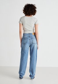 Top gris de manga corta combinado con jeans rectos de tiro alto en azul claro, que cuentan con bolsillos traseros y un parche de cuero beige en la cintura.