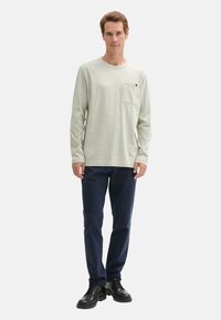 Langärmliges, hellgrünes Hemd mit Brusttasche, kombiniert mit marineblauen Hosen und schwarzen Lederschuhen, stehend vor einem weißen Hintergrund.