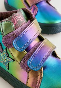 Kolorowe dziecięce buty z holograficznym metalicznym wykończeniem, fioletowymi rzepami i błyszczącą gwiazdką z boku. Gumowa podeszwa.