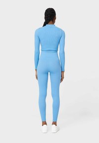 Niebieski zestaw składający się z długiego rękawa z prążkami i legginsów, z dopasowanym krojem, gładką fakturą i wysokim pasem, połączony z białymi sneakersami.