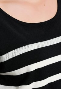 Czarny i biały sweter w paski o miękkiej teksturze, z błyszczącym srebrnym paskiem z cekinów na wysokości klatki piersiowej oraz klasycznym okrągłym dekoltem.