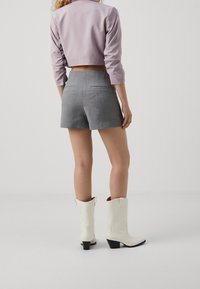 Chaqueta corta de color púrpura claro, pantalones cortos grises ajustados y botas de vaquero blancas con tacón negro. Textura suave con un diseño minimalista.