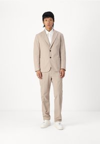 Light beige suit made of textured material with a single-breasted jacket, two pockets, and matching trousers, paired with white sneakers.