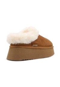 Pantofole di pelle scamosciata marrone con un ampio colletto in pelliccia sintetica color crema e una suola piatta beige. Presenta il marchio sul lato e una suola testurizzata per una maggiore aderenza.
