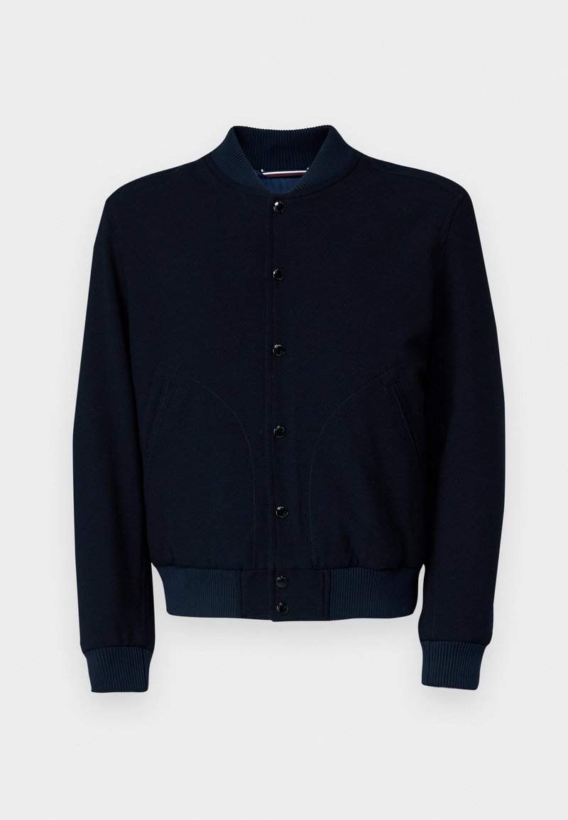 Giacca bomber in maglia blu navy con colletto e polsini a costine, chiusura con bottoni a pressione e due tasche frontali con cuciture curve.