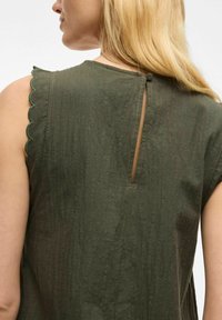 Vestido verde olivo con tejido texturizado, ribete en los hombros con forma de concha y cierre en la parte posterior con ojal. Diseño sencillo con mangas cortas.