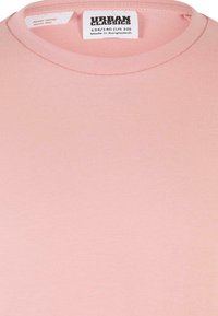 Ljust rosa t-shirt i mjuk bomull, med rund halsringning och tvättetikett med varumärke och storleksinformation.