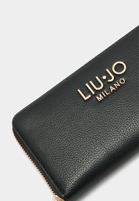 Portafoglio in pelle nera con texture, caratterizzato da un logo metallico dorato "LIU·JO MILANO" e chiusura con zip lungo il bordo.