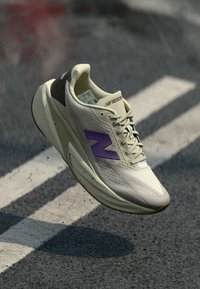 Jasnoszary but sportowy z fioletowymi akcentami, oddychająca siateczka górna, fakturowana powierzchnia, amortyzowana podeszwa i system sznurowania na fakturowanym tle.