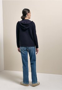 Felpa navy con cappuccio regolabile, abbinata a jeans a gamba dritta azzurri e scarpe beige. Tessuto morbido con una trama liscia.