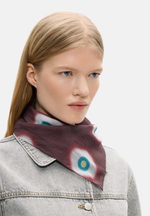 Blondynka o niebieskich oczach ubrana w jasną dżinsową kurtkę i bordo szalik z białymi i niebieskimi okrągłymi wzorami wokół szyi.