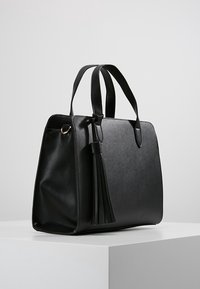 Borsa nera con design strutturato, materiale in ecopelle liscia e un lungo pendente a nappina. Presenta due manici e una forma rettangolare.