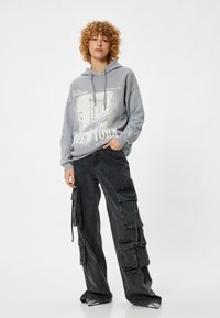 Grijze hoodie met grafische print van een stadslandschap en de tekst "New York"; gecombineerd met zwarte cargo-broeken voorzien van meerdere zakken en trekkoorden.
